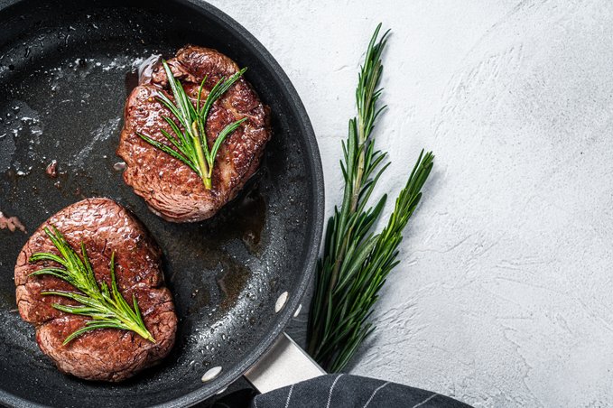 Filet mignon in a pan with a rosemary garnish.
