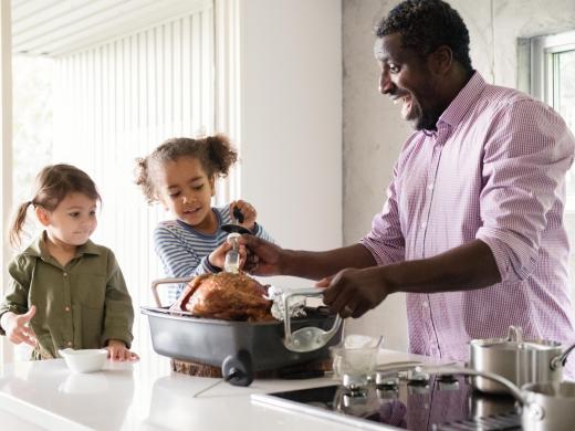 A father bastes a turkey on a counter with help from two young daughters.