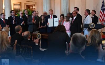 Secretary Azar, Trump, and a group of people standing in front of a crowd at the Putting American Patients First by Making Healthcare More Transparent event