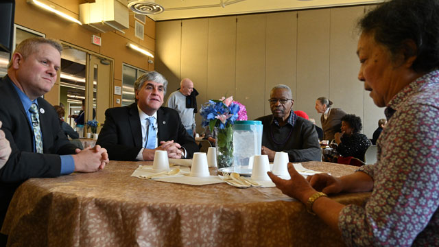 Assistant Secretary Lance Robertson and Deputy Secretary Eric Hargan at a table, speaking with a Walter Reed Community and Senior Center client