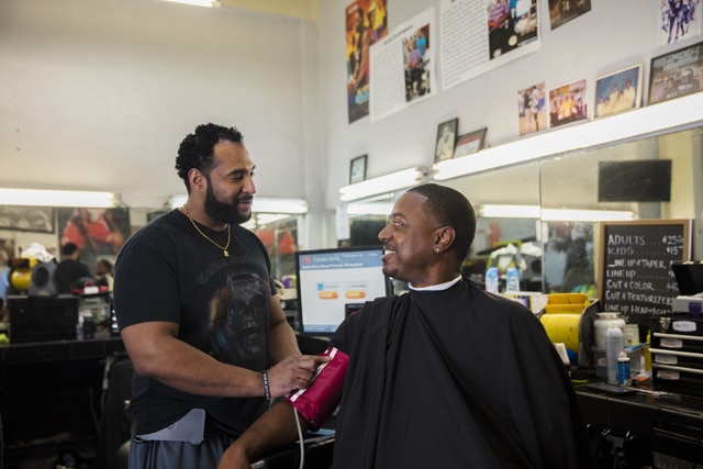 Eric Muhammad (left), owner of A New You Barbershop in Inglewood, California, prepares to measure the blood pressure of long-time customer Marc Sims. Photo credit: Smidt Heart Institute at Cedars-Sinai Medical Center.