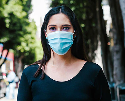 Portrait of a young adult woman with face mask standing outside.