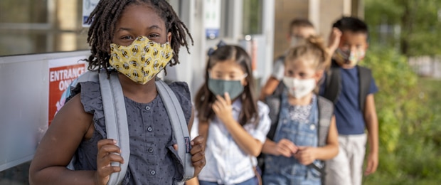 group of elementary school kids wearing masks in line to enter school building