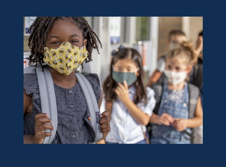 group of elementary school kids wearing masks in line to enter school building