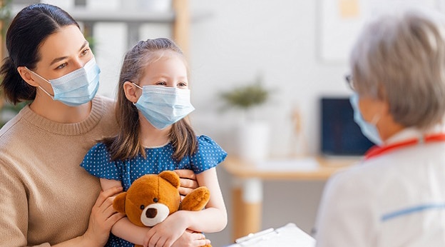 Adult and child interacting with a medical professional. Child is holding a teddy bear.