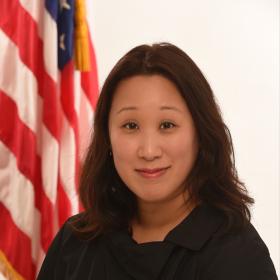 Susan is seated in front of the American flag wearing a black top.