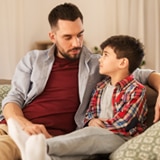 father speaking with young son on couch at home