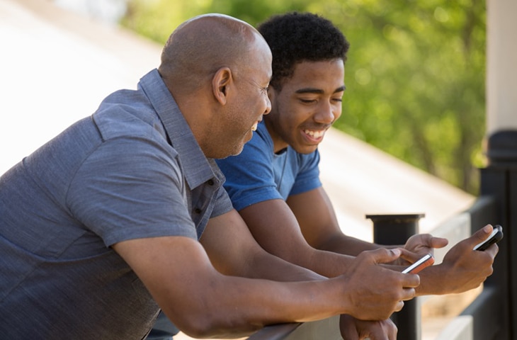 Un hombre y un adolescente hablan con sus teléfonos en la mano