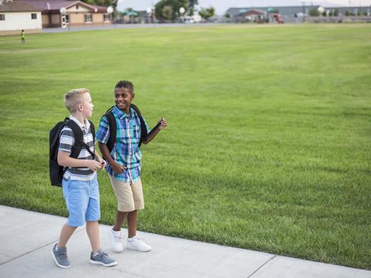 Dos niños diferentes caminan a casa juntos mientras conversan después de la escuela Foto de regreso a clases con diferentes niños usando mochilas en el patio de la escuela