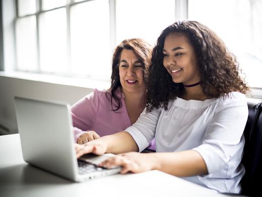 Adult mentor helping a teen mentee work on a laptop.